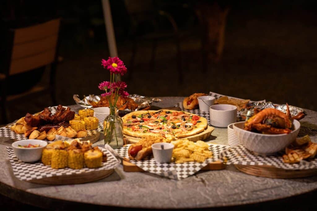 A diverse dinner spread with pizza, corn, ribs, and snacks on an outdoor table setting.